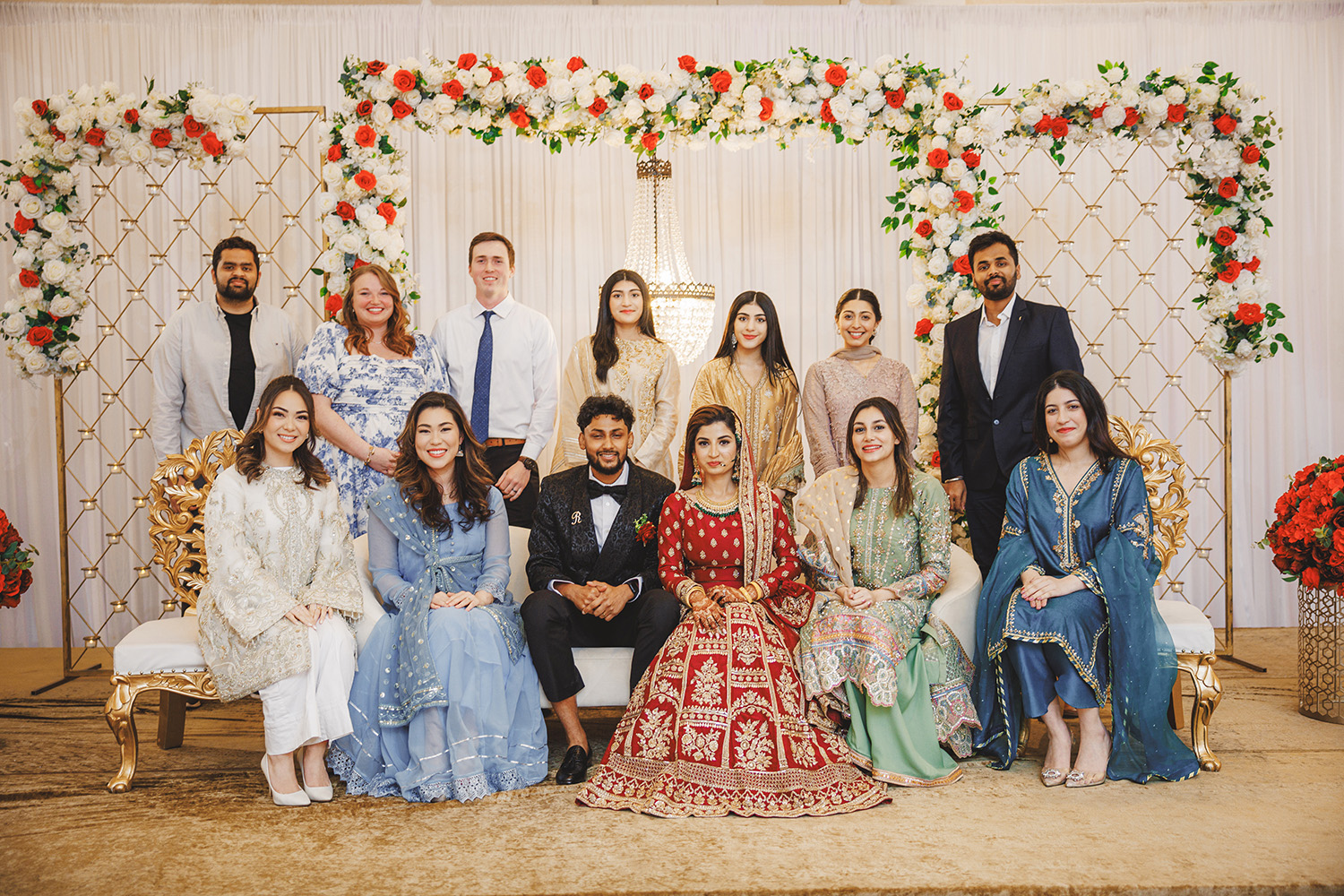 A group of people, dressed in formal and traditional attire, pose for a charming family photo in front of a floral backdrop, capturing cherished moments through photography.