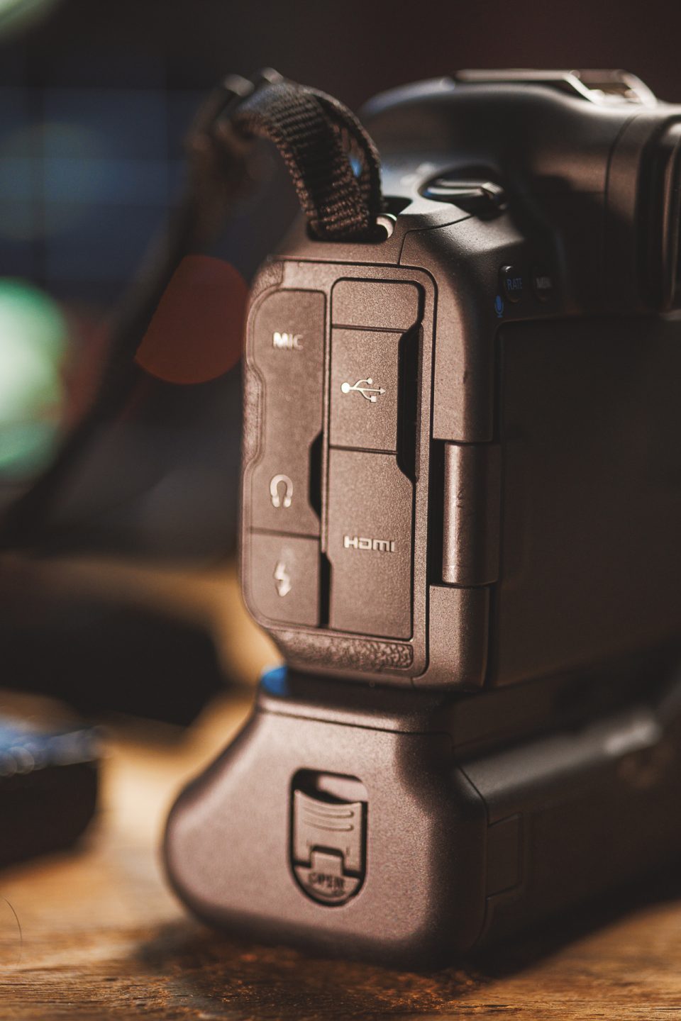 Close-up of a Canon R5 Mark ii camera showing its side ports, including mic, headphone, USB, and HDMI connections. In this review shot, the camera grip and strap are also visible, highlighting features essential for real-world use.