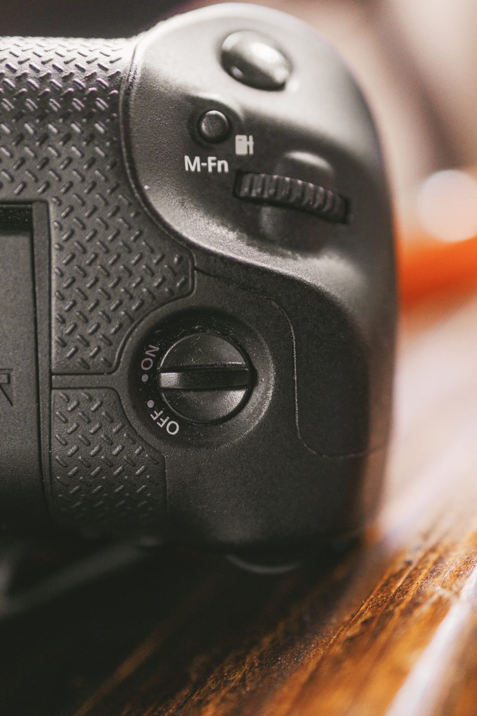 Close-up of a black camera grip showing a textured surface, a dial with "OFF" and "ON" settings, and an "M-Fn" button next to a control wheel.